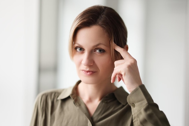 Serious woman puts index finger on temple looking in camera female entrepreneur thinks of ideas