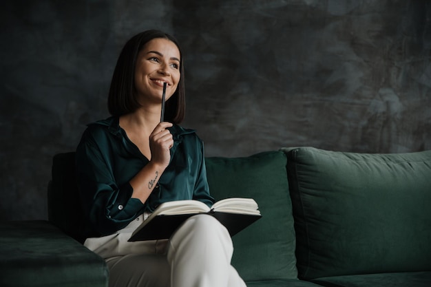 Serious woman sitting on green couch in loft living room working from home creative female designer