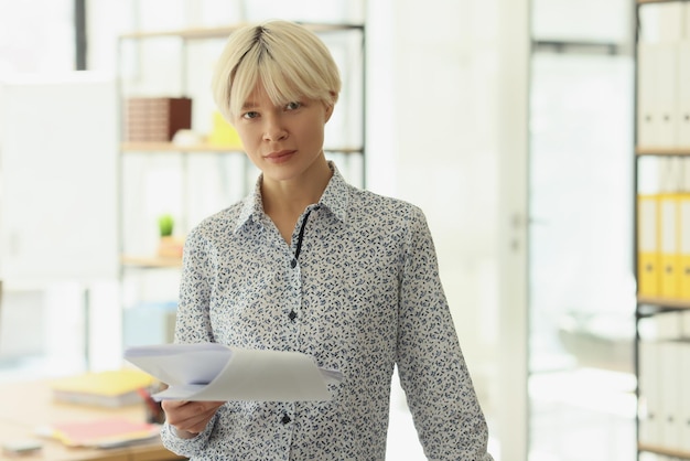 Serious woman with short dyed blonde hair holds clipboard with project details looking in