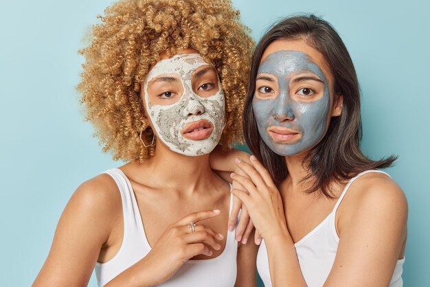 Serious women apply beauty facial masks undergo perfect\
treatment to help with skincare concerns try to remove excess oils\
reduce signs of aging dressed casually isolated over blue\
background