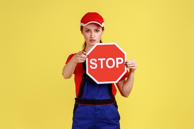 카메라를 가리키는 빨간색 정지 도로 표지판을 들고 있는 심각한 작업자 여성