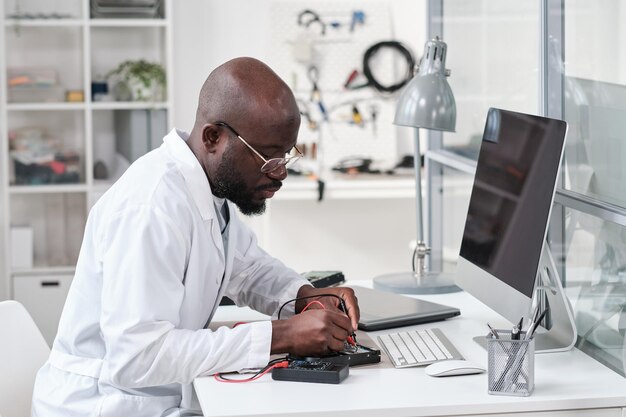 Serious young african repairman in whitecoat soldering circuit board