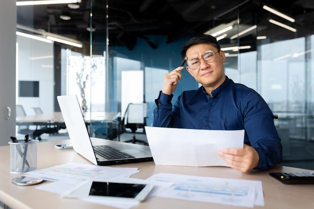 Serious young asian architect designer engineer sitting at the desk in the office holding documents