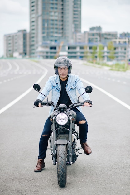 Serious young Asian man in helmet riding motorcycle on highway