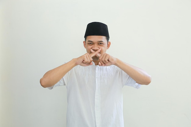 彼の口に指を組んで立っているアラビア語の衣装を着ている深刻な若いアジアのイスラム教徒の男性