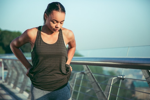 Serious young athlete standing outdoors and pulling her sporty trousers up