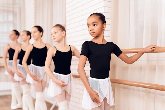 Serious Young Ballerinas Stand along Ballet Barre.