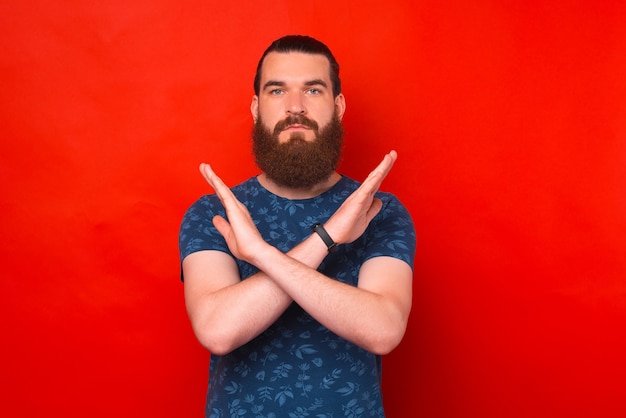 Photo serious young bearded man is crossing hands for the stop or enough sign.