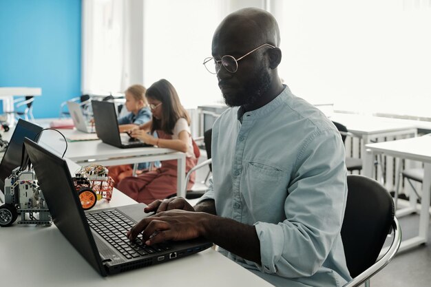 Giovane uomo di colore serio in camicia casual seduto davanti al computer portatile a lezione