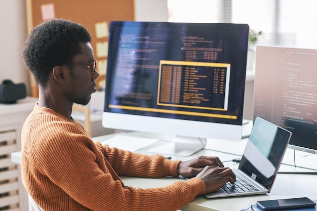 Serious young black man in warm orange sweater concentrated on\
coding