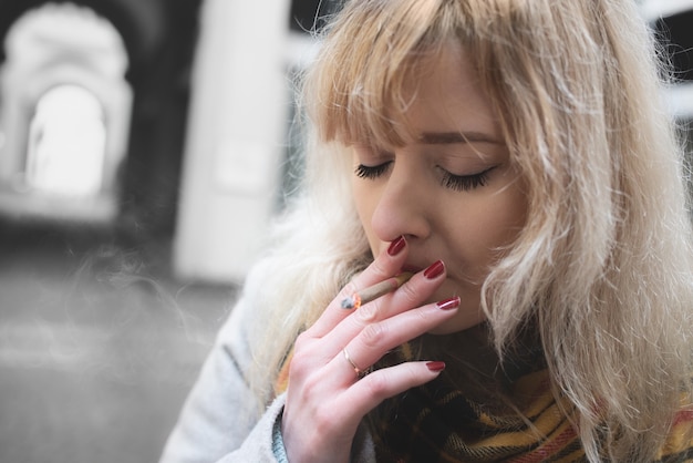 Serious young blond woman on gray background , smoking with closed eyes