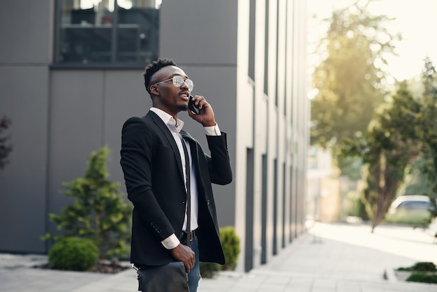 Foto giovane uomo d'affari serio in abito nero in piedi e a parlare al cellulare vicino al centro commerciale