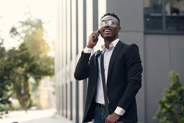 Foto giovane uomo d'affari serio in abito nero in piedi e a parlare al cellulare vicino al centro commerciale