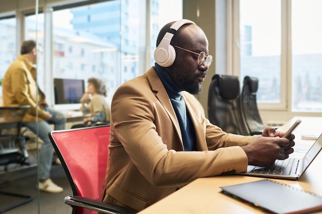 Serious young businessman choosing new track from playlist in mobile phone