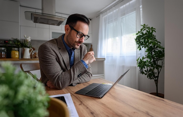 Serious young businessman looking at laptop and thinking business ideas while working from home