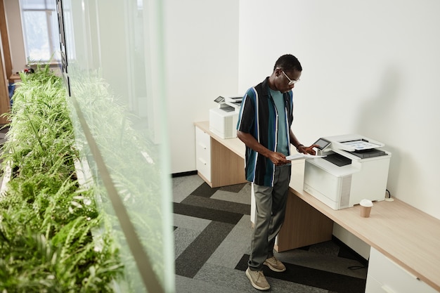 Photo serious young businessman stading at photocopier and checking reports he printed for meeting