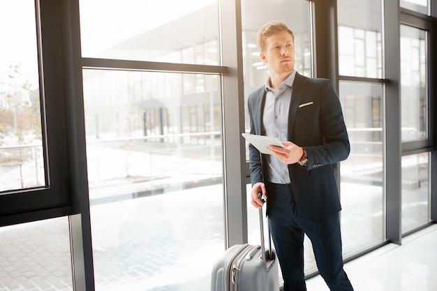 Serious young businessman stand at window in airport hall