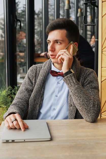 Serious young businessman wearing blue shirt sitting in a cafe while talking on the phone Look away
