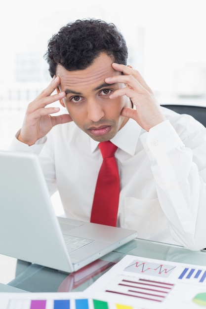 Serious young businessman with laptop and graphs