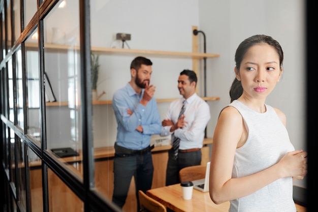 Серьезная молодая деловая женщина подслушивает разговор своих коллег-мужчин в конференц-зале