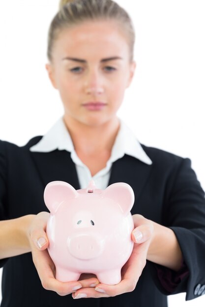 Serious young businesswoman holding pink piggy bank