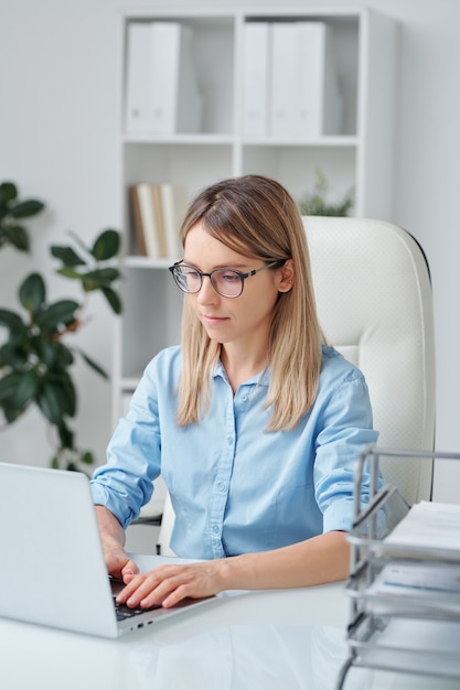 Seria giovane donna d'affari o segretaria d'ufficio che esamina i dati sul display del laptop, fa un piano di lavoro o prepara una presentazione