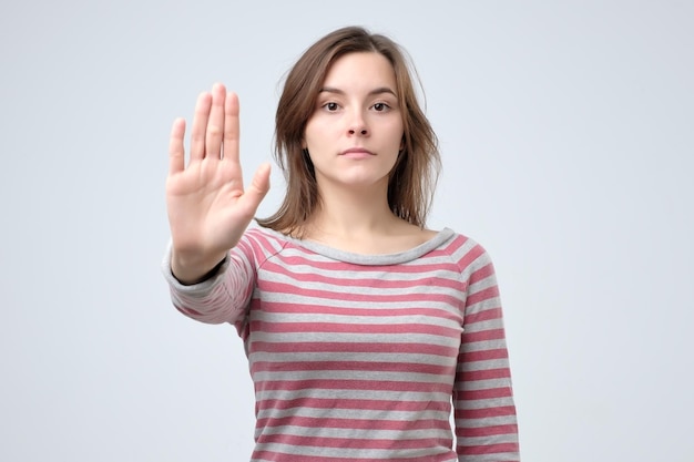 Serious young caucasian woman showing stop gesture with her hand