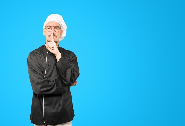 Serious young chef asking for silence gesturing with his finger