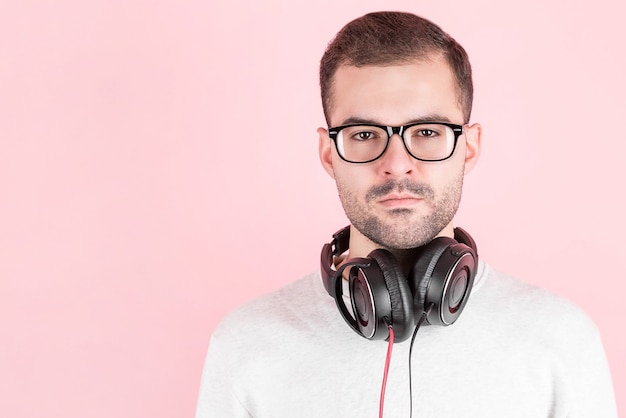 Serious young cute kid listening to music in big white headphones on pink background, in white sweatshirt, world dj day