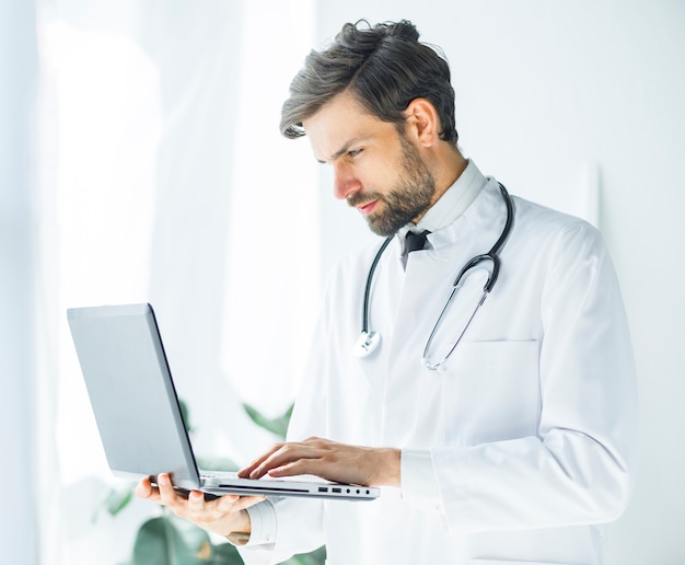 Serious young doctor browsing laptop