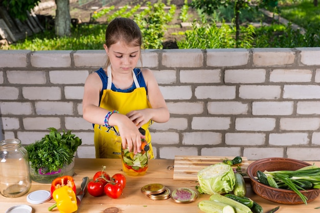 Serious young girl bottling a variety of farm fresh vegetables in glass jars working at a large outdoor table in a self sufficiency concept