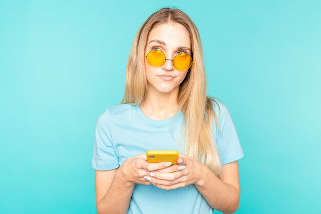 Serious young girl using smartphone and thinking on blue