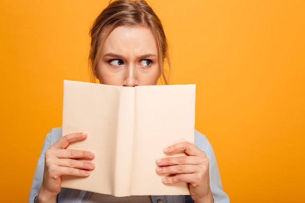 Serious young lady student covering face with book