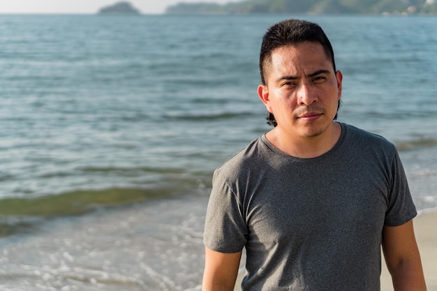 Giovane uomo latino serio che guarda la telecamera sulla spiaggia, concetto di stile di vita urbano