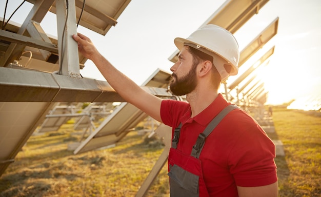 Serious young male technician examining photovoltaic panels at station