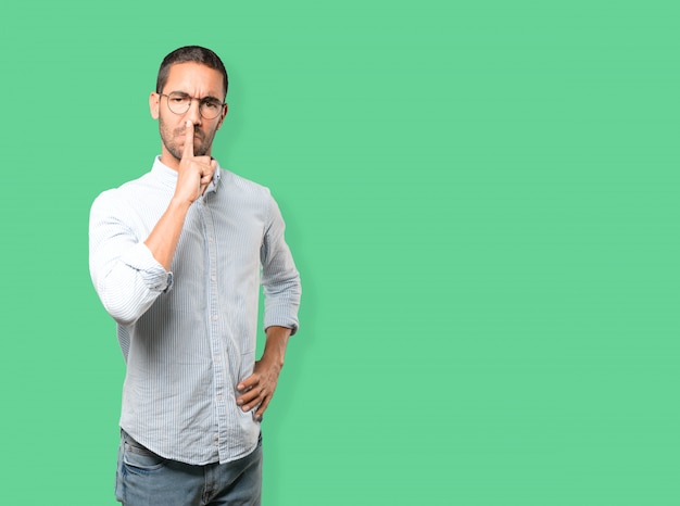 Serious young man asking for silence gesturing with his finger