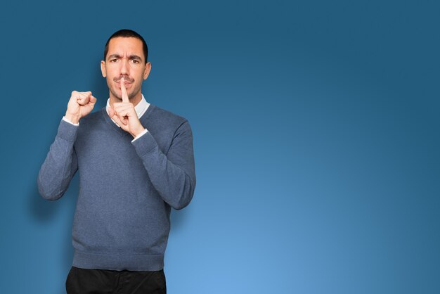 Serious young man asking for silence gesturing with his finger