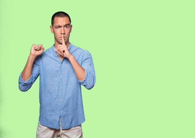 Serious young man asking for silence gesturing with his
finger