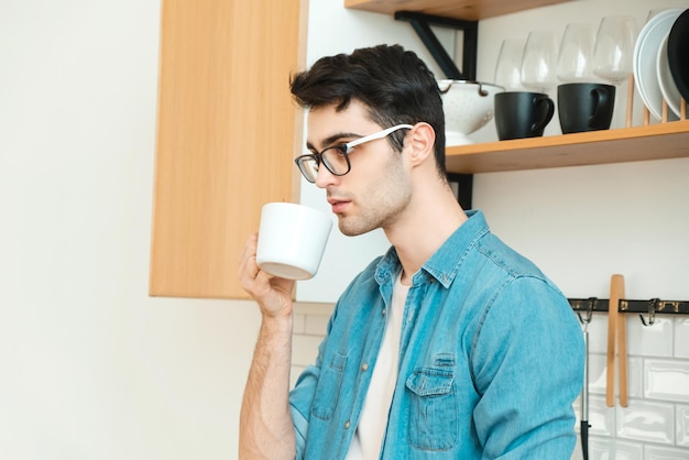 Serious young man drinking tea or coffee in the kitchen worrying about the situation in the world
