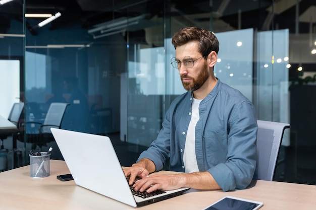 Serious young man freelancer designer it specialist works concentratedly in the office coworking