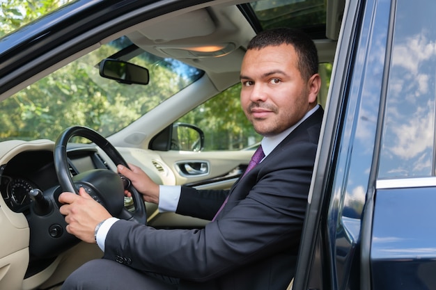 Serious young man of Middle Eastern appearance in a business suit is driving an expensive car