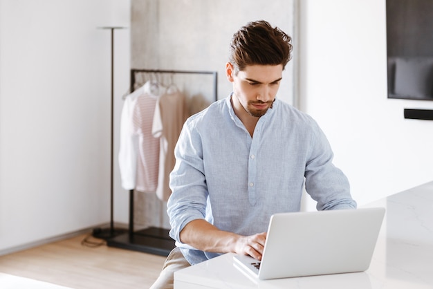 Serious young man in shirt using laptop computer