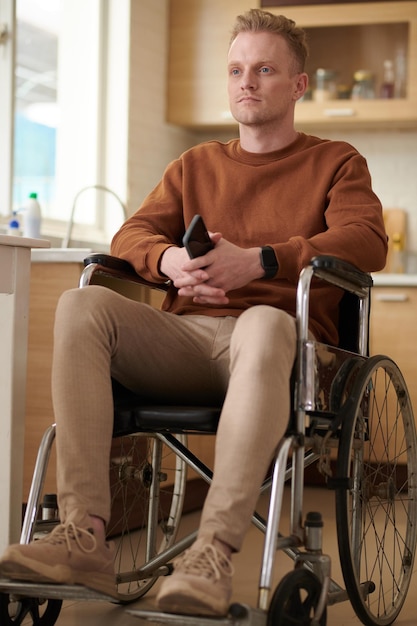 Серьезный молодой человек, сидящий в инвалидной коляске