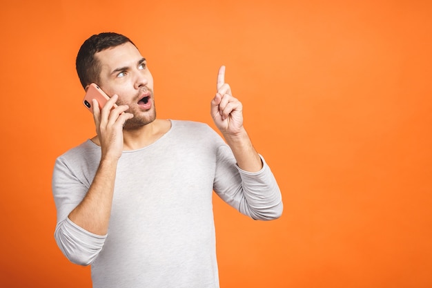 Serious young man talking on mobile isolated on orange background