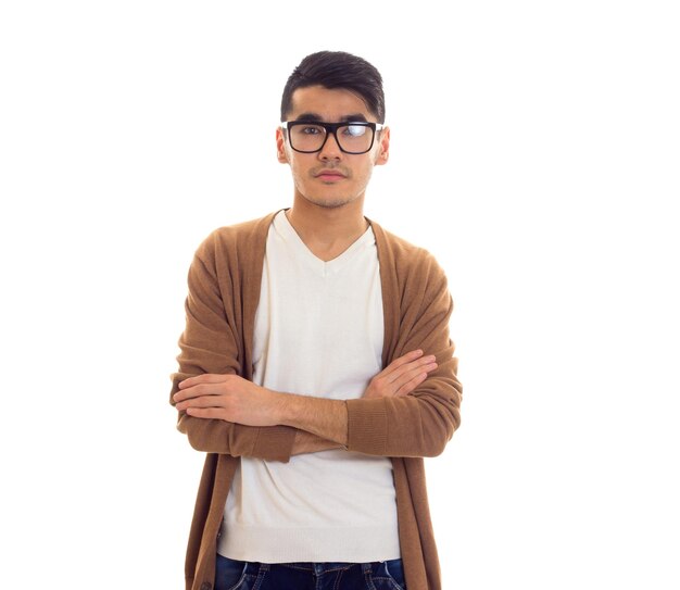 Serious young man with black hair in white Tshirt brown cardigan and blue jeans with black glasses