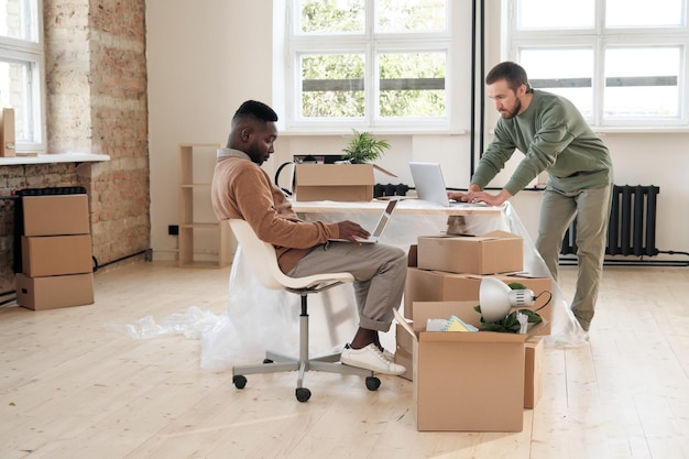 Serious young multiethnic project managers in sweater analyzing
online files on computers while work