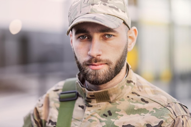 A serious young soldier standing in the street wearing a cap an