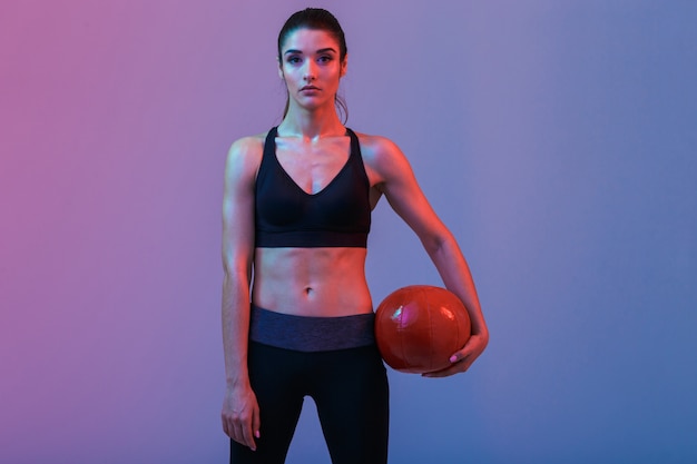 Serious young sports woman standing with ball