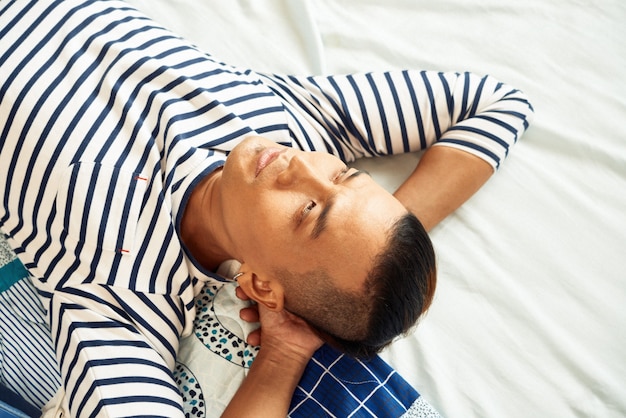 Serious young Vietnamese man relaxing on bed, dreaming and overthinking life