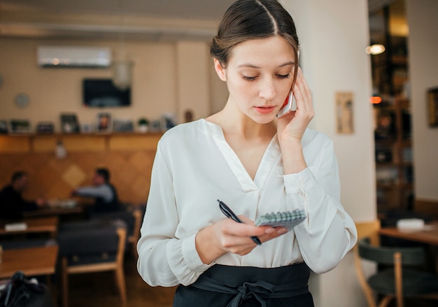 Serious young waitress stand in restraunt and talk on phone